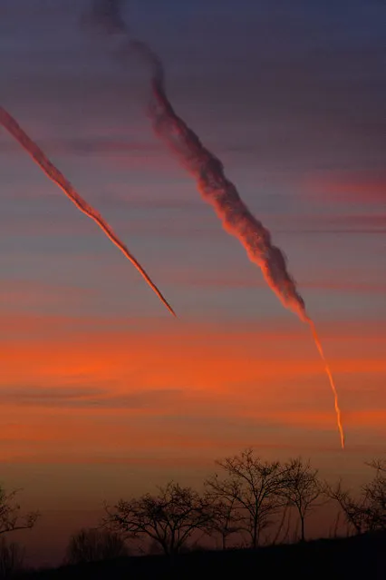 The contrails of two airplanes fade in the sky as the rising sun adds a spectatcular color cast to the landscape in Hajdusamson, 232 kilometers east of Budapest, on 13 January 2015 morning. (Photo by Zsolt Czegledi/EPA)