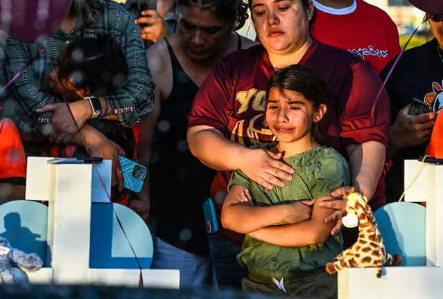 Gabriella Uriegas, a soccer teammate of Tess Mata who died in the shooting, cries while her mother Geneva Uriegas holds her as they visit a makeshift memorial outside the Uvalde County Courthouse in Texas on May 26, 2022. Texas police faced angry questions May 26, 2022 over why it took an hour to neutralize the gunman who murdered 19 small children and two teachers in Uvalde, as video emerged of desperate parents begging officers to storm the school. (Photo by Chandan Khanna/AFP Photo)