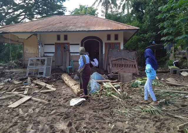 Indonesian women walk past a house damaged by flood in Waiwerang, on Adonara Island, East Nusa Tenggara province, Indonesia, Tuesday, April 6, 2021. Rescuers in remote eastern Indonesia were digging through the debris of a landslide Tuesday in search of people believed to be buried in one of several disasters brought on by severe weather in the Southeast Asian nation and neighboring East Timor. (Photo by Rofinus Monteiro/AP Photo)