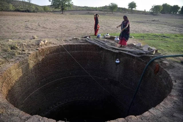 In this picture taken on June 9, 2022, women collect water from a well in Agrotha village, in Tikamgarh, Madhya Pradesh. As the monsoon storms bear down on India, a dedicated group of women hope that after years of backbreaking labour, water shortages will no longer leave their village high and dry. (Photo by Sanjay Kanojia/AFP Photo)