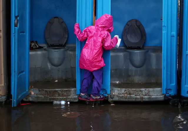 A migrant girl, part of a caravan of thousands from Central America trying to reach the United States, tries to avoid flooded ground by holding on to the door of a toilet after heavy rainfall in a temporary shelter in Tijuana, Mexico, November 29, 2018. (Photo by Hannah McKay/Reuters)