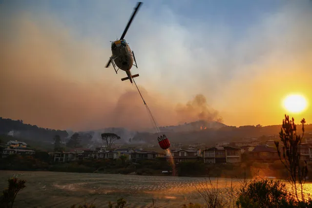 A helicopter carries water to a fire in the Helderberg mountains around Somerset West, South Africa, 04 January 2017. (Photo by Nic Bothma/EPA)