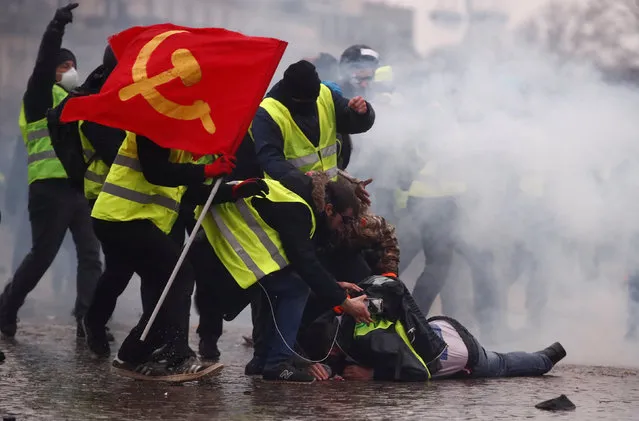 Protesters wearing yellow vests help a person injured by a water cannon during a demonstration by the “yellow vests” movement near the Arc de Triomphe in Paris, France, January 12, 2019. (Photo by Christian Hartmann/Reuters)