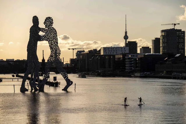 Two stand-up paddlers pass the sculpture “Molecule Man” by American sculptor Jonathan Borofsky on the Spree as the sun sets, in Berlin, Germany, Wednesday, July 7, 2021. (Photo by Christophe Gateau/dpa via AP Photo)