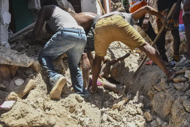 Several men work to rescue the body of a girl buried in the rubble of a house in the aftermath of an earthquake in Les Cayes, Haiti, Saturday, August 14, 2021. (Photo by Duples Plymouth/AP Photo)