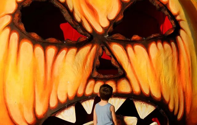 A kid looks at a giant Halloween pumpkin made from papier-mache in Valletta, Malta on October 24, 2022. (Photo by Darrin Zammit Lupi/Reuters)