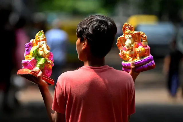 A boy carries idols of the elephant-headed Hindu god Ganesha outside a workshop ahead of the Ganesh Chaturthi festival in New Delhi on September 6, 2021. (Photo by Money Sharma/AFP Photo)