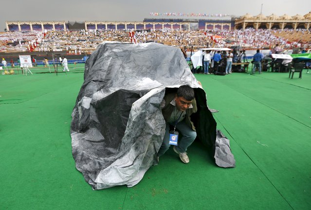 An attendee comes out from a plastic sheet which was used to take shelter from rains at the venue of World Culture Festival on the banks of a river in New Delhi, India, March 11, 2016. (Photo by Adnan Abidi/Reuters)