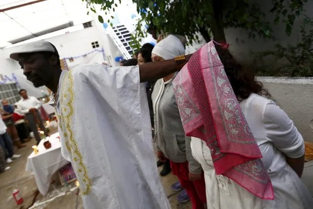 A voodoo priest holds a handkerchief on the head of a woman during a voodoo ceremony in honor of Kouzen Zaka, also known as St. Isidro, in Mexico City, May 2, 2015. (Photo by Edgard Garrido/Reuters)