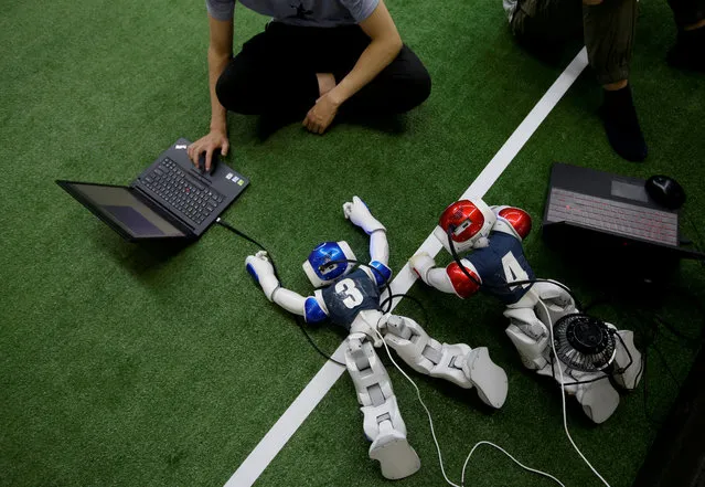 A participant from SJTU team works next to robot soccer players, which are being charged, at the break of a competition against SPQR team during the RoboCup Asia-Pacific Tianjin Invitational Tournament 2019, in the side event of the World Intelligent Congress in Tianjin, China on May 17, 2019. (Photo by Jason Lee/Reuters)