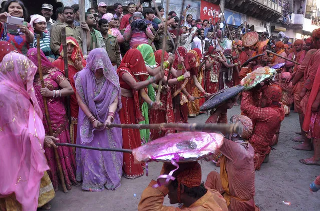 A group of women beat men holding a shield over their heads during “Lathmar Holi” at the village of Barsana in the northern Indian state of Uttar Pradesh March 9, 2014. (Photo by K. K. Arora/Reuters)