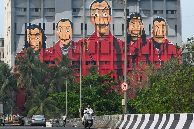 Commuters drive past a mural depicting characters from the Spanish TV show “Money Heist” in Mumbai on December 15, 2021. (Photo by Punit Paranjpe/AFP Photo)
