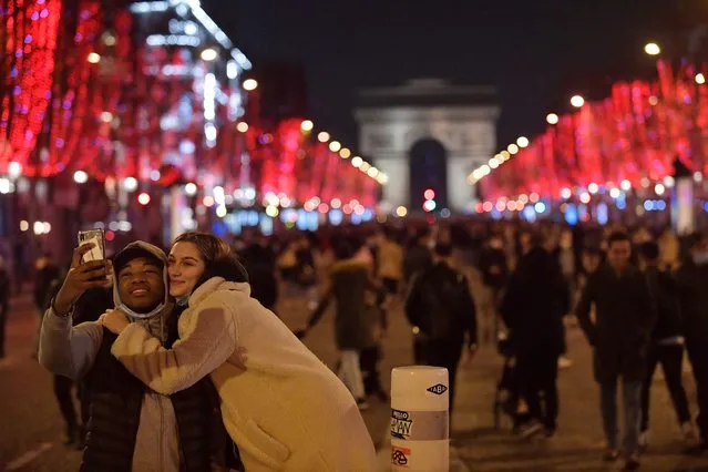 A couple takes a selfie picture along the Champs-Elysees Avenue on New Year's Eve, on December 31 2021. Since December 31, 2021, the protective face mask is mandatory for pedestrians in Paris and other cities to prevent the spread of the Covid-19 (coronavirus) pandemic. (Photo by Julien de Rosa/AFP Photo)