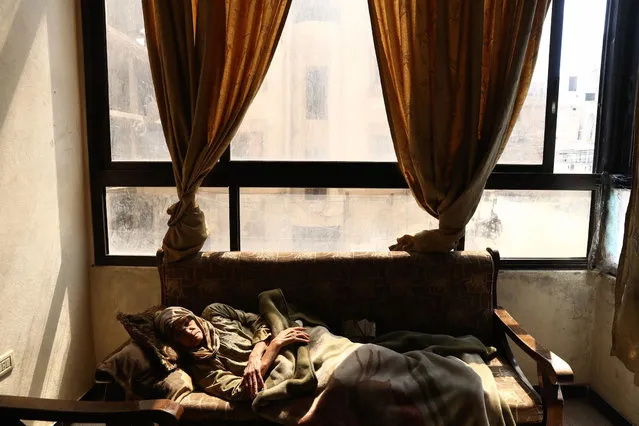 Syrian Umm Ahmad, a seventy- three- year old widow, who was displaced from the al- Maliha area due to the ongoing fighting, is seen inside her home in the rebel- controlled town of Kafr Batna, in the eastern Ghouta region on the outskirts of the capital Damascus, on March 26, 2017. Um Ahmad, suffers from many diseases and isn' t able to walk. Access to proper health care is very limited for Syrians living in poverty and under the siege. (Photo by Abd Doumany/AFP Photo)