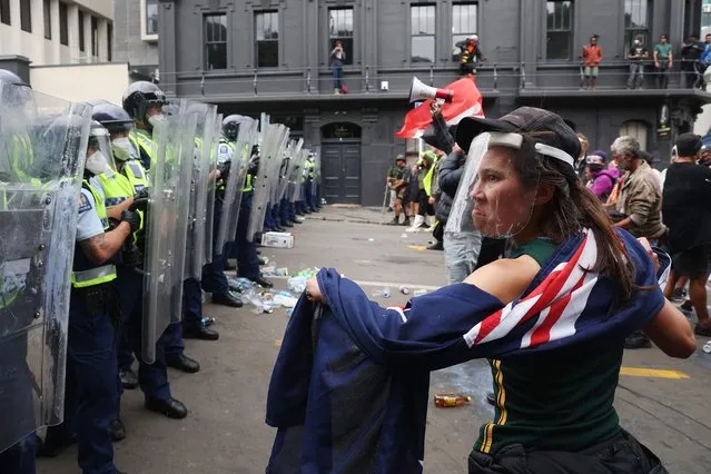A woman looks at police standing guard as they move in to clear protesters from Parliament grounds in Wellington on March 2, 2022, during demonstrations against Covid-19 vaccine mandates and restrictions. (Photo by Marty Melville/AFP Photo)