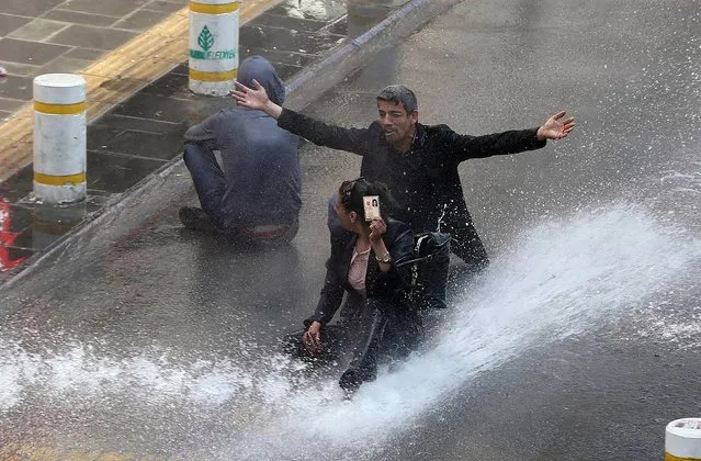 A woman shows her identity card next to another protestor as riot police uses water cannons during clashes after hundreds of people tried to reach the city's main Kizilay Square to celebrate May Day in Ankara on May 1, 2014. Earlier, riot police in Istanbul used water cannon and tear gas against thousands of protesters who tried to defy a May Day ban on demonstrations, injuring at least 50 people. (Photo by Adem Altan/AFP Photo)