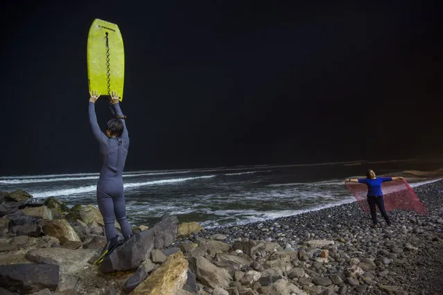 In this April 21, 2017 photo, Renato de Negri, 15, lifts his boogie board to signal to a fellow surfer in Pacific Ocean waters that he has returned to shore, at La Pampilla beach, in Lima, Peru. Pampilla beach does not attract sharks, unlike some beaches in the United States and Australia. The greatest danger faced by night surfers is that they can crash into each other, blinded by the powerful floodlights. (Photo by Rodrigo Abd/AP Photo)
