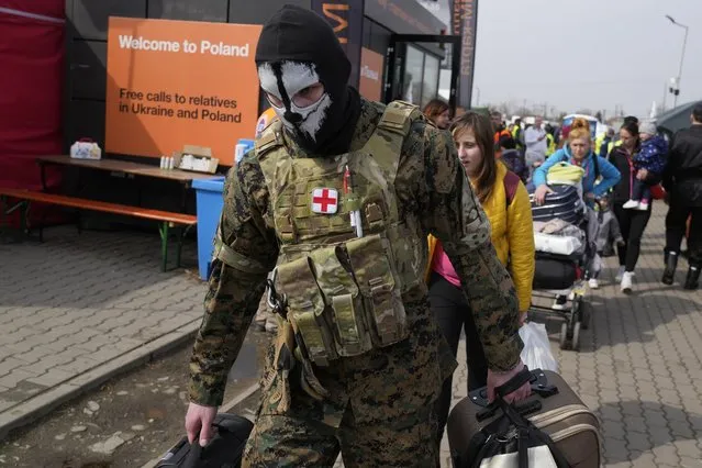 A man in military uniform carries bags as Ukrainian refugees depart from the border crossing in Medyka, southeastern Poland, on Wednesday, March 30, 2022. (Photo by Sergei Grits/AP Photo)