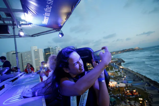 An Israel woman takes photos as she eats dinner on a platform held by a crane at a height of 40 meters during a food festival in Tel Aviv, Israel May 24, 2016. (Photo by Baz Ratner/Reuters)