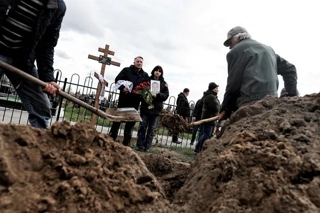 Maria, 13, holds a photograph of her father Yurii Alekseev, 50, a territorial defence member who according to his family was killed by Russian soldiers, as she mourns him with her godfather Igor Tarkovskii, 60, during his funeral, amid Russia's invasion of Ukraine, at the cemetery in Bucha, Kyiv region, Ukraine on April 26, 2022. (Photo by Zohra Bensemra/Reuters)