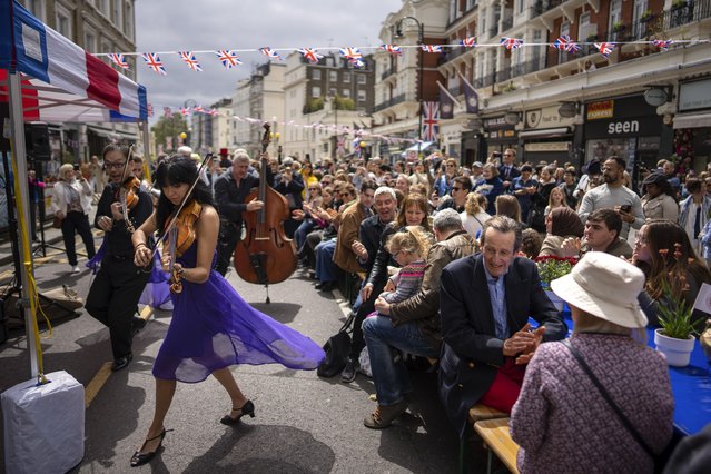 Musicians play their instruments as people sit at long tables to eat their lunch as part of the Big Lunch celebration in London, Sunday, May 7, 2023. The Big Lunch is part of the weekend of celebrations for the Coronation of King Charles III. (Photo by Emilio Morenatti/AP Photo)