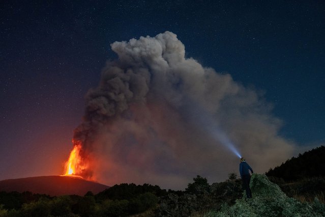 A person looks on as lava and plumes of smoke rise from a crater of Mount Etna, Europe's most active volcano, Italy on July 15, 2024. (Photo by Giuseppe Di Stefano/Etna Walk via Reuters)