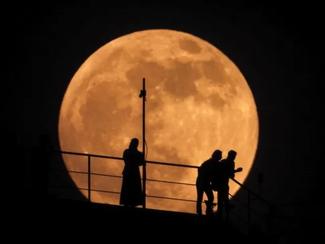 People are silhouetted as an almost full moon rises above the sky in Grozny, Russia, Sunday, May 15, 2022. (Photo by Musa Sadulayev/AP Photo)