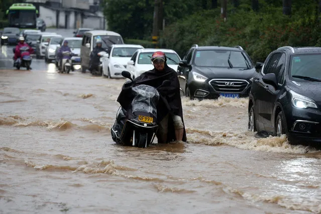 A man wades through a flooded street with a vehicle during heavy rain in Huangshan, Anhui Province, China, June 19, 2016. (Photo by Reuters/Stringer)