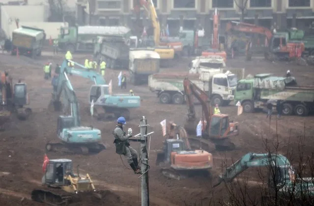 An electrician sets up wiring while construction workers drive excavators at the site of a new 1,000-bed field hospital being built to accommodate the increasing number of coronavirus patients on January 24, 2020 in Wuhan, Hubei Province, China. The hospital is set to be completed by February 3, 2020. (Photo by Getty Images)