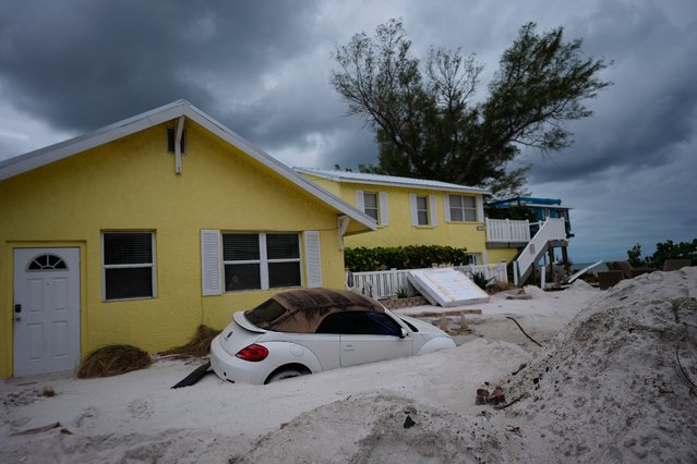 A car sits half-buried in sand as Bradenton Beach, Fla., which was in the process of cleaning up after Hurricane Helene, as Hurricane Milton approaches on Anna Maria Island, Tuesday, October 8, 2024. (Photo by Rebecca Blackwell/AP Photo)