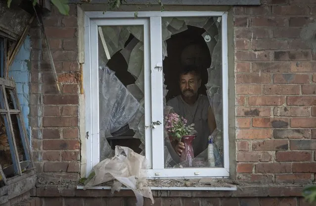 A local resident places a vase with flowers on a broken window in his house damaged by the Russian shelling in Bakhmut, Donetsk region, Ukraine, Sunday, June 26, 2022. (Photo by Efrem Lukatsky/AP Photo)