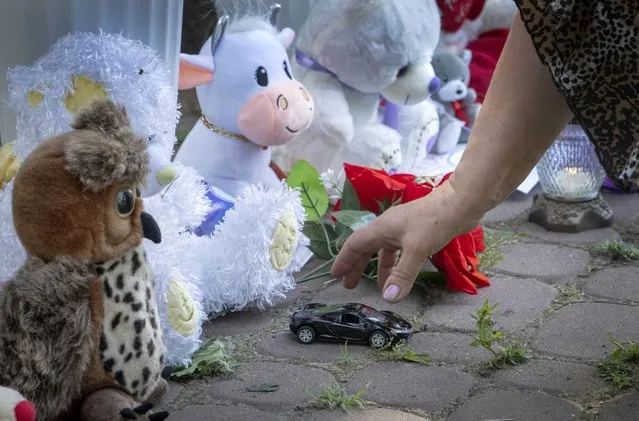 A woman lays a toy car near to tributes for the victims of the Russian rocket attack at a shopping center in Kremenchuk, Ukraine, Wednesday, June 29, 2022. (Photo by Efrem Lukatsky/AP Photo)