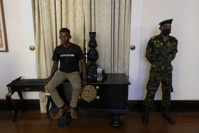 Sri Lanka army officer stands guard as a protester sits on the table inside the official residence of president Gotabaya Rajapaksa fourth days after it was stormed by anti government protesters in Colombo in Colombo, Sri Lanka, Wednesday, July 13, 2022. (Photo by Rafiq Maqbool/AP Photo)