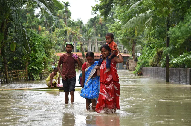A woman carries her child as she and others wade through a flooded road in Jakhalabandha area in Nagaon district, Assam, August 14, 2017. (Photo by Anuwar Hazarika/Reuters)