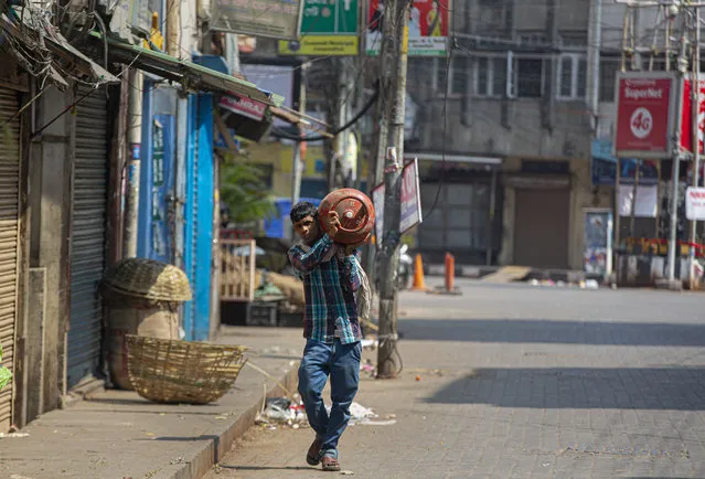 An Indian man carries a cooking gas cylinder through a deserted road during a lockdown in Gauhati, India, Wednesday, March 25, 202. (Photo by Anupam Nath/AP Photo)