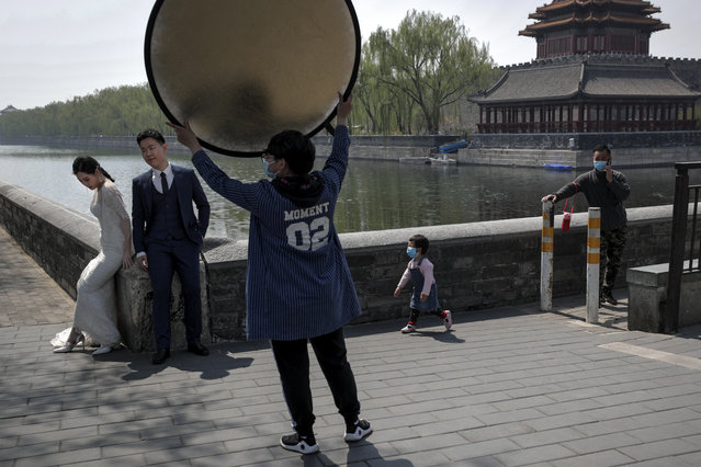 A child wearing a protective face mask to help prevent the spread of the new coronavirus runs towards a bride and groom during a pre-wedding photo shoot in front of the Turret of the Forbidden City which remain closed following the new coronavirus outbreak in Beijing, Monday, April 6, 2020. China on Monday reported a few dozen new cases of coronavirus infection while no new confirmed or suspected cases in the epicenter city of Wuhan, where a 14-week lockdown is due to be lifted on Wednesday. (Photo by Andy Wong/AP Photo)