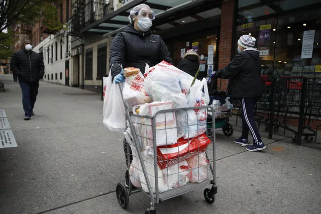 A shopper wears a face mask and gloves as she leaves a grocery store with a loaded cart Saturday, April 18, 2020, in the Harlem neighborhood of the Manhattan borough of New York during the coronavirus outbreak. (Photo by John Minchillo/AP Photo)