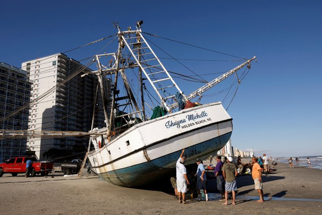 Workers and owners of a large shrimping boat prepare their vessel for towing back into the water after it was swept ashore by hurricane Ian in Myrtle Beach, South Carolina, U.S., October 1, 2022. (Photo by Jonathan Drake/Reuters)