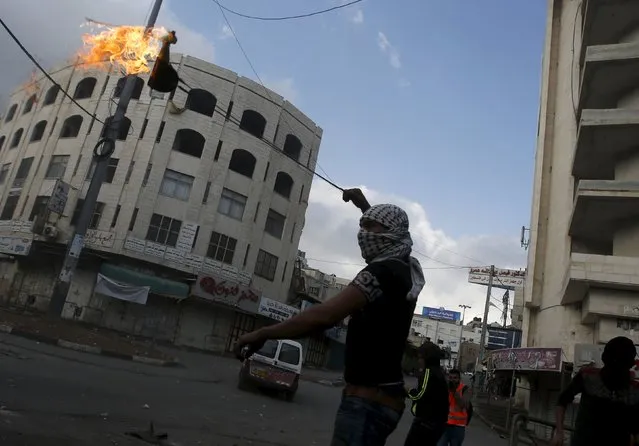 A masked Palestinian uses a sling to throw a molotov cocktail at Israeli troops during clashes in the West Bank city of Hebron October 9, 2015. (Photo by Mussa Qawasma/Reuters)