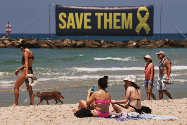 A banner, referring to the hostages being held by Hamas in the Gaza Strip, is displayed on the beach as people sunbath and walk along the sand in Tel Aviv, Israel, Friday, July 4, 2025. (Photo by Oded Balilty/AP Photo)