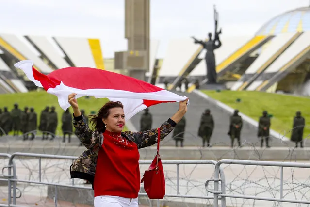 A woman waves an old Belarusian national flag as she a police line in front of a WWII memorial, during an opposition rally to protest the official presidential election results in Minsk, Belarus, Sunday, September 27, 2020. (Photo by TUT.by via AP Photo)