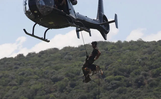 In this photo taken Wednesday, November 26 2014 a handler and his dog abseil from a helicopter, in a simulated exercise showing training at an academy run by the Paramount Group, near Rustenburg, South Africa. (Photo by Denis Farrell/AP Photo)