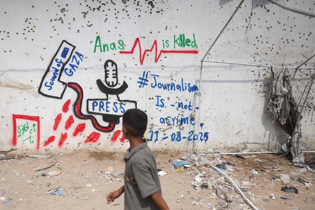 A Palestinian boy looks at a graffiti on the wall at the site where a deadly Israeli strike destroyed an Al Jazeera tent and killed six journalists, at the Al-Shifa Hospital in Gaza City on August 12, 2025. Condemnations poured in from the United Nations, the EU and media rights groups on August 11, after an Israeli strike killed an Al Jazeera news team in Gaza, as Palestinians mourned the journalists and Israel accused one of them of being a Hamas militant. (Photo by Bashar Taleb/AFP Photo)