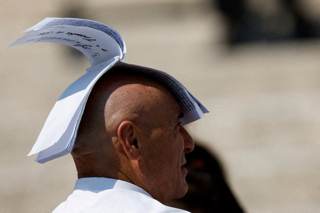 A man shields himself from the sun with a book, as he attends a general audience held by Pope Leo XIV in St. Peter's Square, at the Vatican, on August 6, 2025. (Photo by Remo Casilli/Reuters)