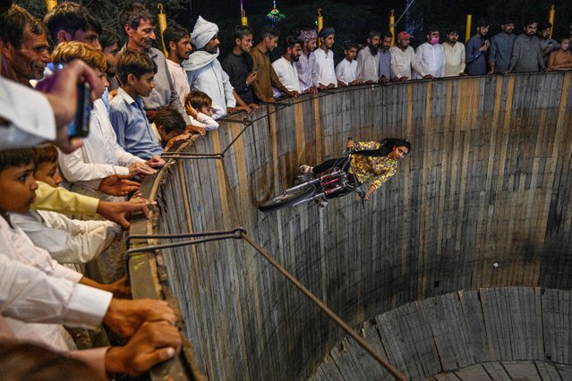 This photograph taken on May 11, 2024 shows Fatima Noor, a stunt girl, performing in a “Wall of Death” during an annual mela or carnival at a Sufi shrine in Shah Jiwana, a town in the Jhang district of Pakistan's Punjab province. Rhythmic drums and spirited dancing are once again bringing life to the shrines of Pakistan's saints, where festivals were long stifled by jihadist violence. As the harvest season ends and schools finish for the summer, villagers climb atop tractor trolleys, buses, and rickshaws to head to the annual celebrations at Sufi shrines dotted across the country. (Photo by Farooq Naeem/AFP Photo)