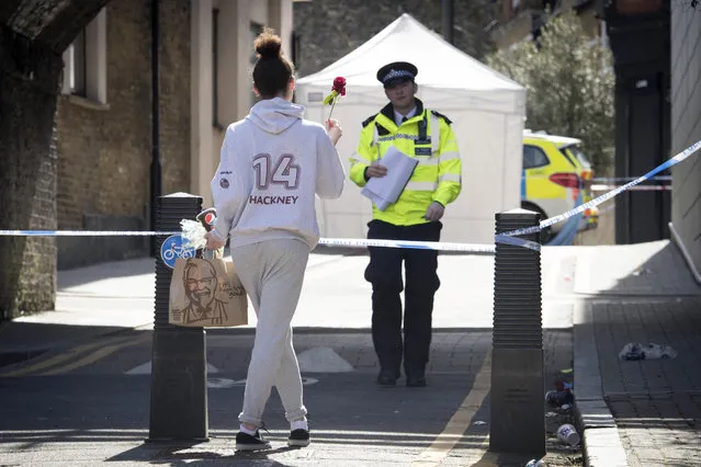 A woman carries a flower to a crime scene in Link Street, Hackney, east London, Thursday April 5, 2018. This week, 18-year-old Israel Ogunsola became London's 53rd murder victim of 2018. The British capital is being shaken by a spike in deadly violence, much of it involving young people caught up in gang feuds. (Photo by Stefan Rousseau/PA Wire via AP Photo)