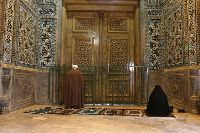 A cleric and a woman pray behind a closed door of Masoume shrine in the city of Qom, some 80 miles (125 kilometers) south of the capital Tehran, Iran, Monday, March 16, 2020. On Monday, Iran closed the Masoume shrine, a major pilgrimage site in the city of Qom, the epicenter of the country's new coronavirus outbreak. Authorities were already restricting access and barring pilgrims from kissing or touching the shrine, but it had remained open. (Photo by AP Photo)