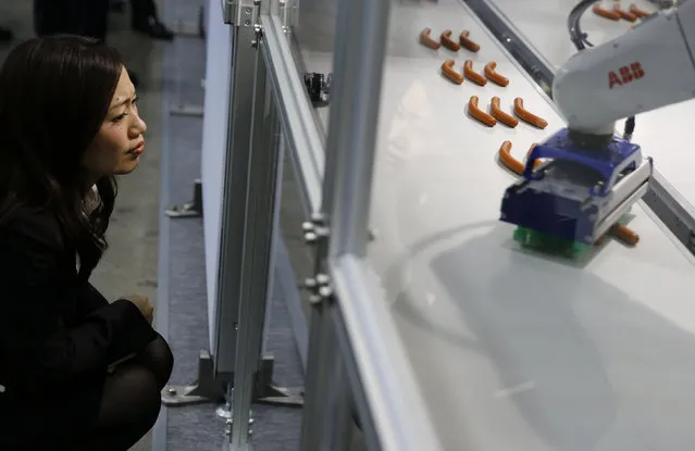 A woman looks at an ABB robot picking up sausages from a conveyor belt at the International Robot Exhibition in Tokyo, Japan December 2, 2015. (Photo by Thomas Peter/Reuters)