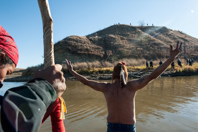 People protest against the building of a pipeline near the Standing Rock Indian Reservation while police officers stand on the opposite shore of a river near Cannonball, North Dakota, U.S. November 2, 2016. (Photo by Stephanie Keith/Reuters)