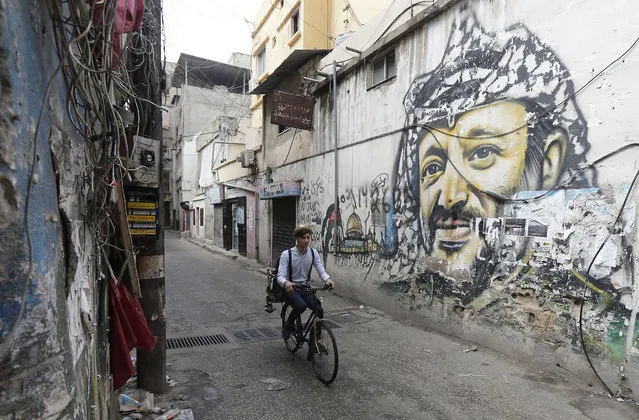 Mohammed, a Lebanese roaming barber, better known as “Abo Tawila”, rides his bicycle in a street on the outskirts of the Palestinian refugee camp Burj al-Barajneh, south of the capital Beirut on May 29, 2018. On the wall is a mural painting of the late Palestinian leader Yasser Arafat. Inspired by roaming street vendors in Beirut, 18 years-old Abo Tawila (the tall one in Arabic), decided to use his bicycle to set up his business. He works mainly in popular neighbourhoods in Beirut and its souther suburbs. (Photo by Joseph Eid/AFP Photo)